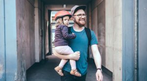 Happy father carrying daughter wearing cycling helmet on footpath